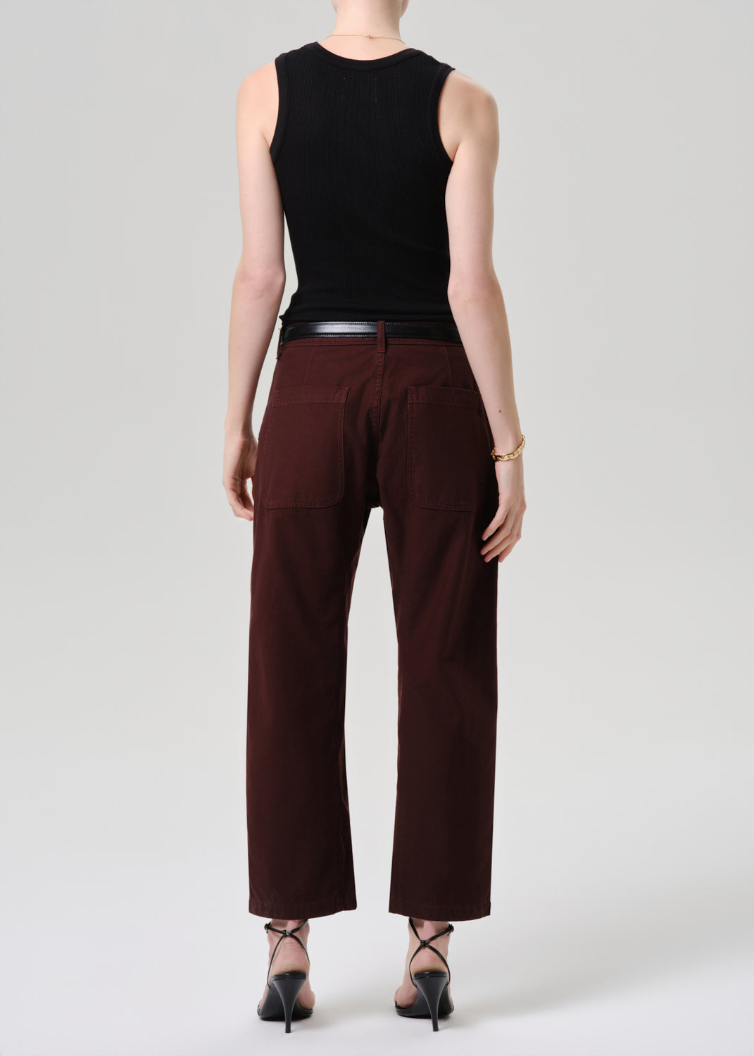 Person wearing a black sleeveless top and brown pants on a grey  background