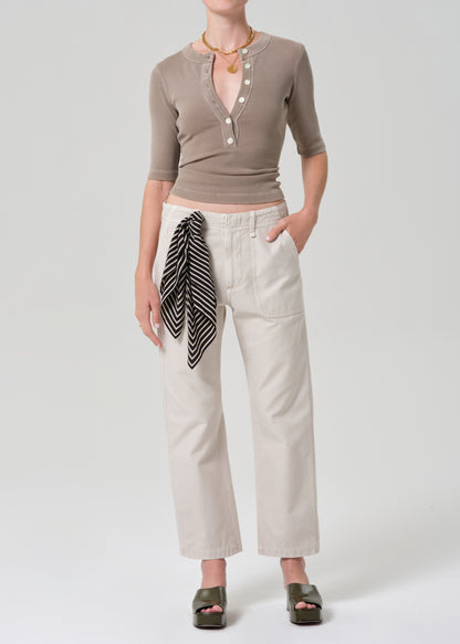 Person wearing a brown top and beige pants with a grey background