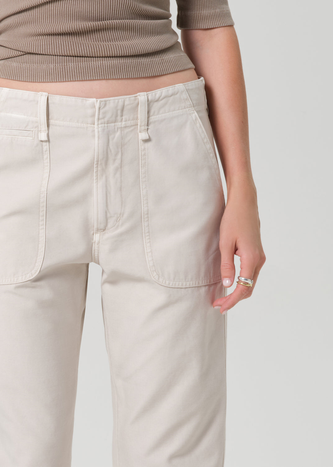 Person wearing a brown top and beige pants on a grey background