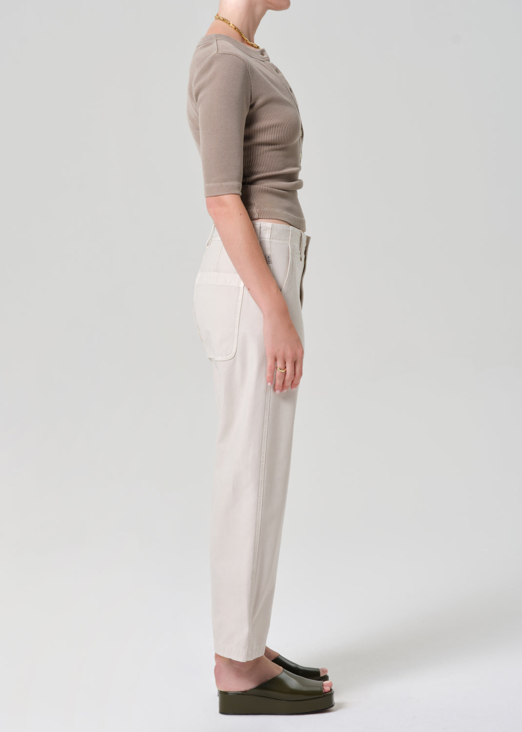 Person wearing a brown top and beige pants on a grey background