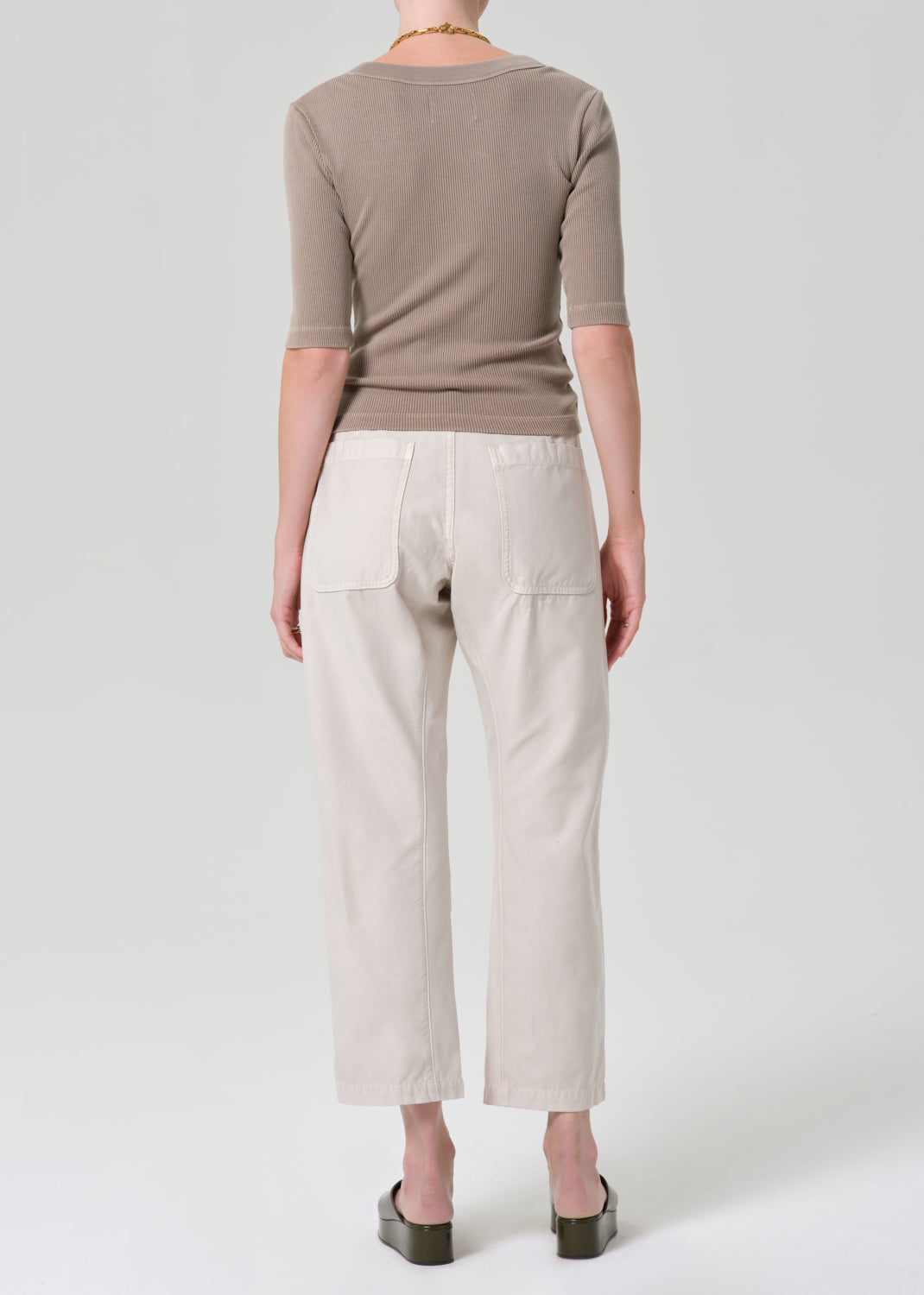 Person wearing a brown top and beige pants on a grey background
