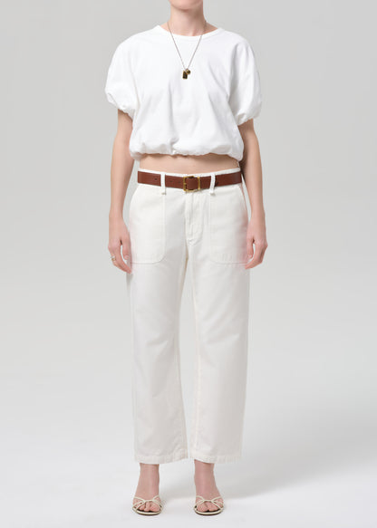 Person wearing a white top and white pants with a brown belt on a light gray background