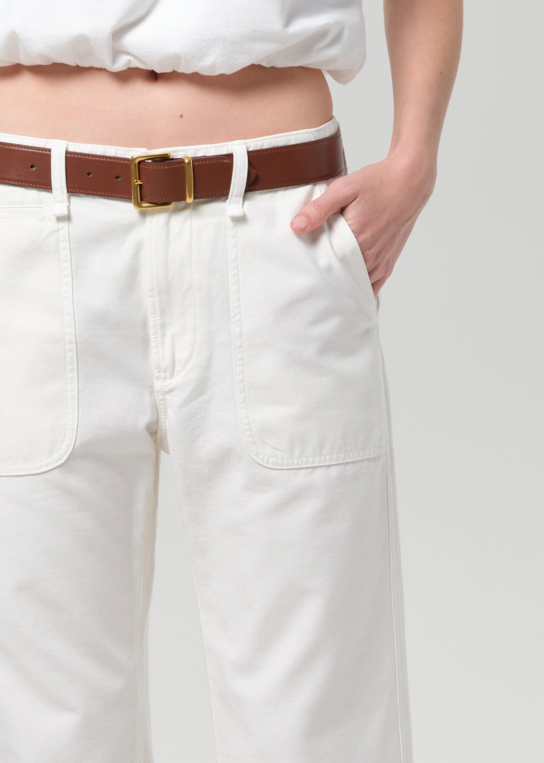 White pants with a brown belt and gold buckle on a plain background