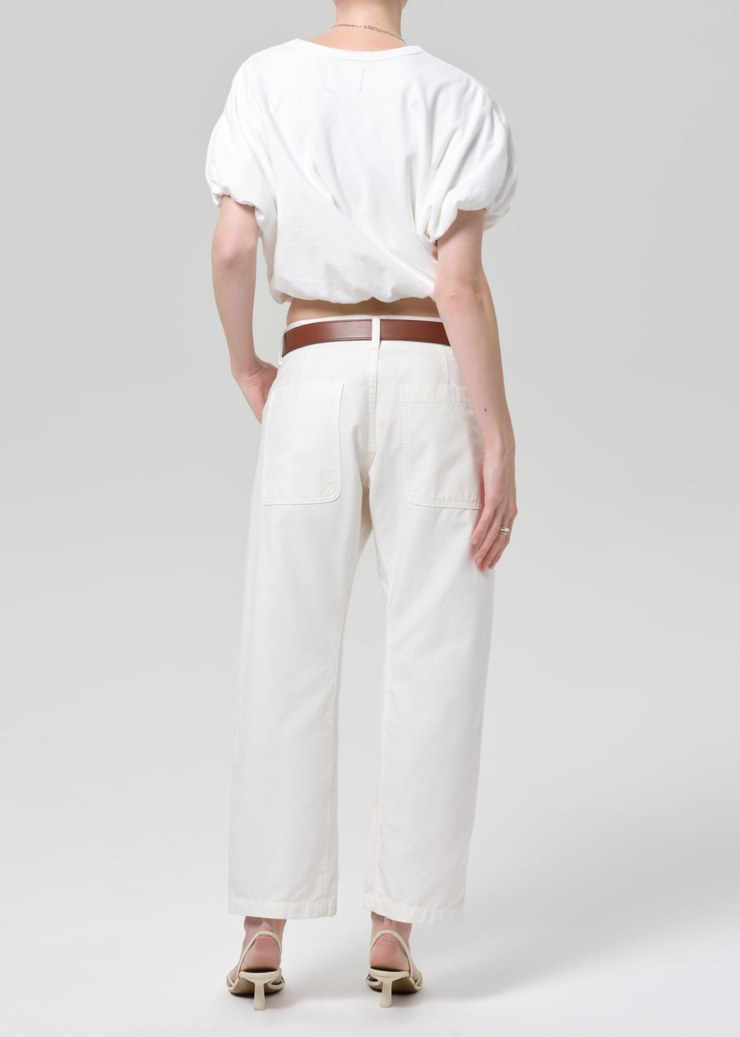 Person wearing a white outfit with a brown belt on a plain background