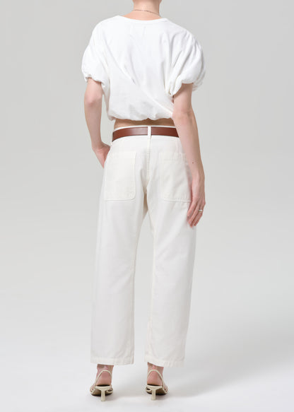 Person wearing a white outfit with a brown belt on a plain background