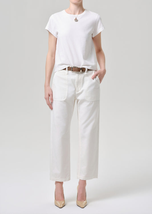 A model wearing a white short-sleeve crewneck t-shirt, white cropped wide-leg pants with front patch pockets, a brown leather belt, and beige pointed-toe heels, standing against a grey background.