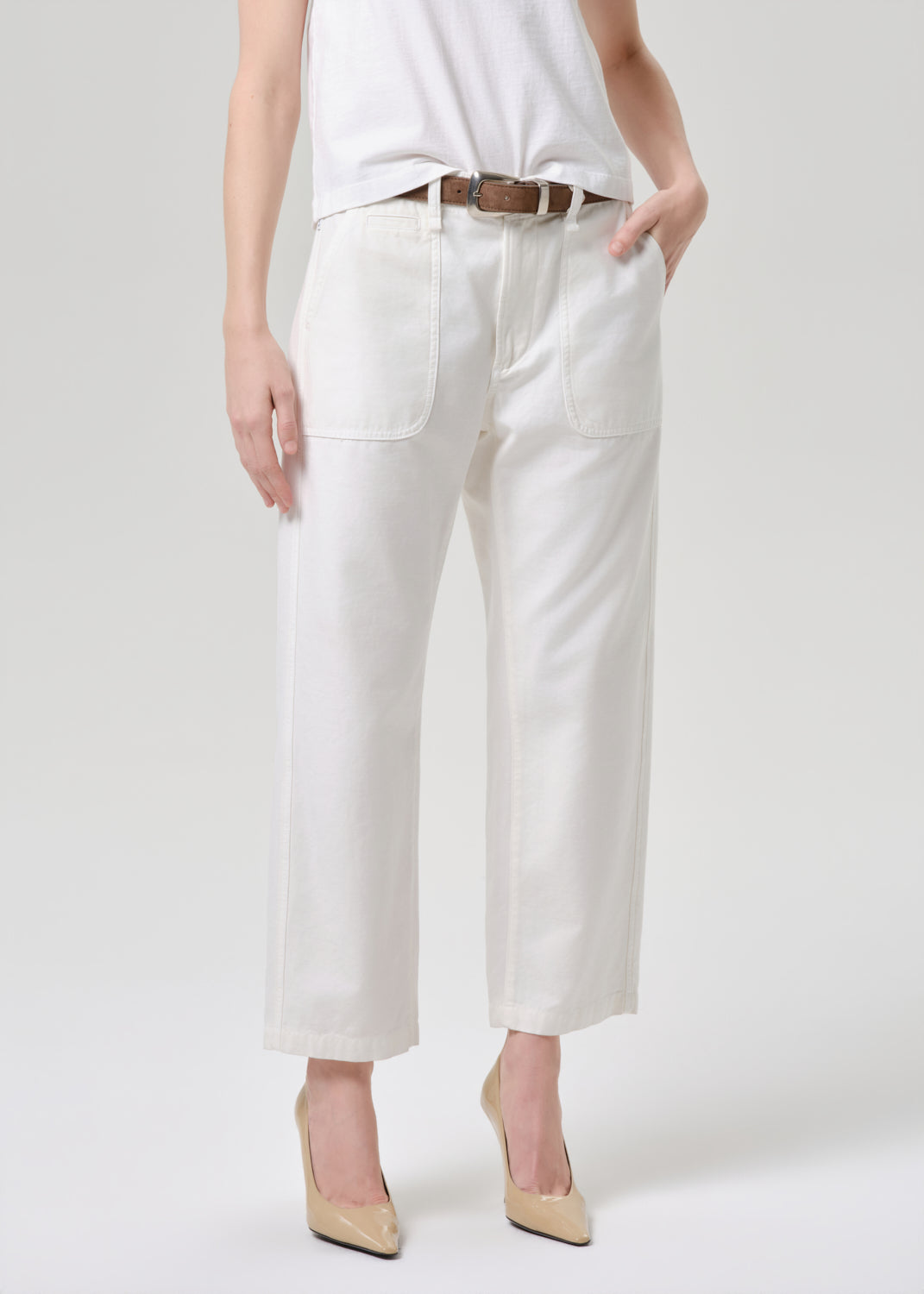 A model wearing off-white cropped wide-leg jeans with a brown belt, paired with a white top and beige heels, shown from the waist down on a grey background.