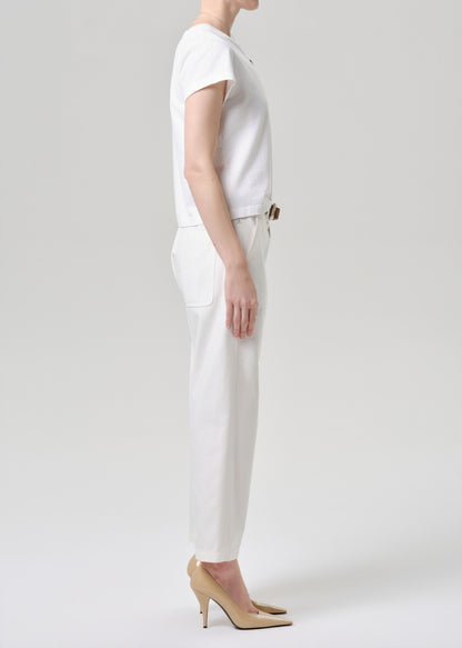 A model shown in profile wearing a white short-sleeve top, white trousers, and beige high heels against a grey background.