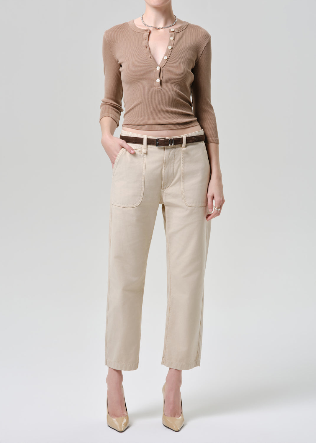 Person wearing a brown long-sleeve top and beige pants on a grey background