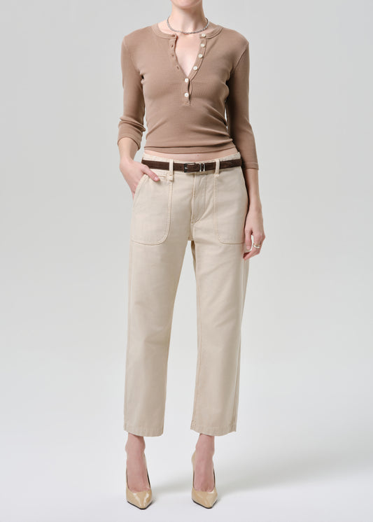 Person wearing a brown long-sleeve top and beige pants on a grey background