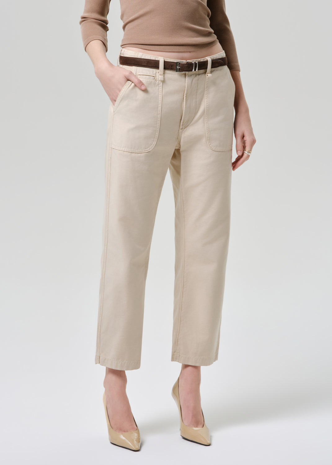 Person wearing beige pants and a brown top on a grey background