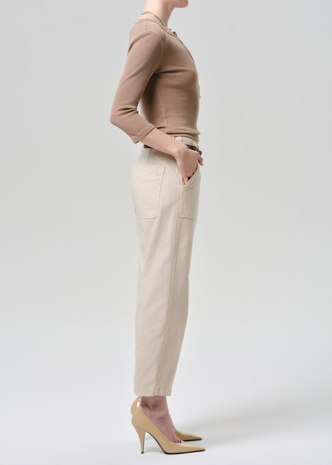 Person wearing a brown top and beige pants on a grey background