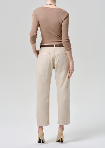 Person wearing a brown long-sleeve top and beige pants on a grey background