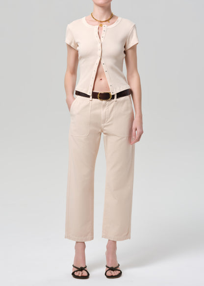 Person wearing a light peach outfit with a belt on a grey background