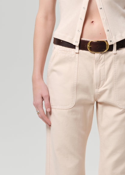 Person wearing a light peach outfit with a belt on a grey background