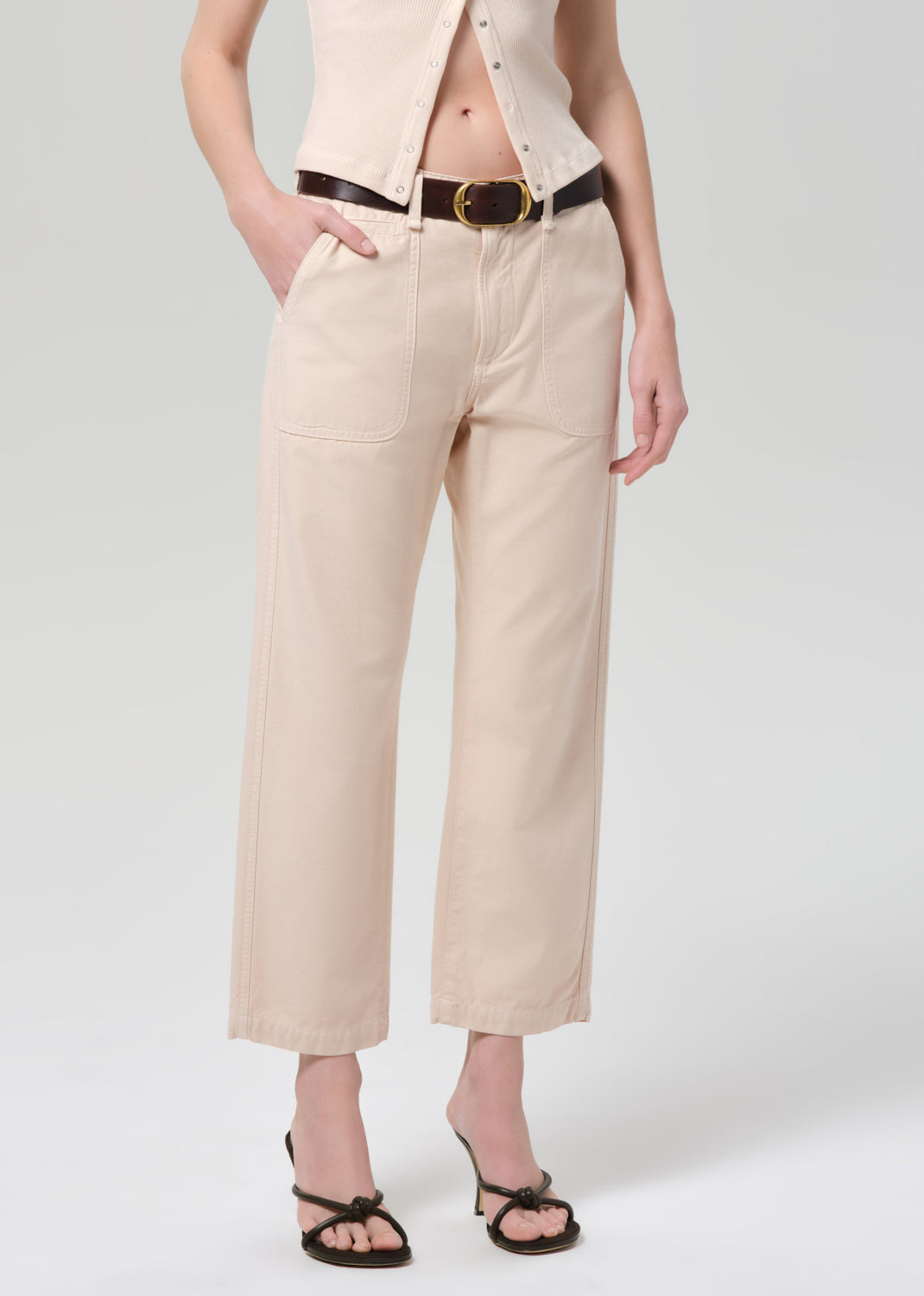 Person wearing a light peach outfit with a belt on a grey background