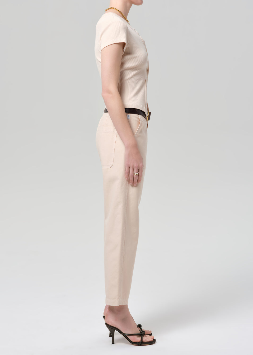 Person wearing a light peach outfit with a belt on a grey background