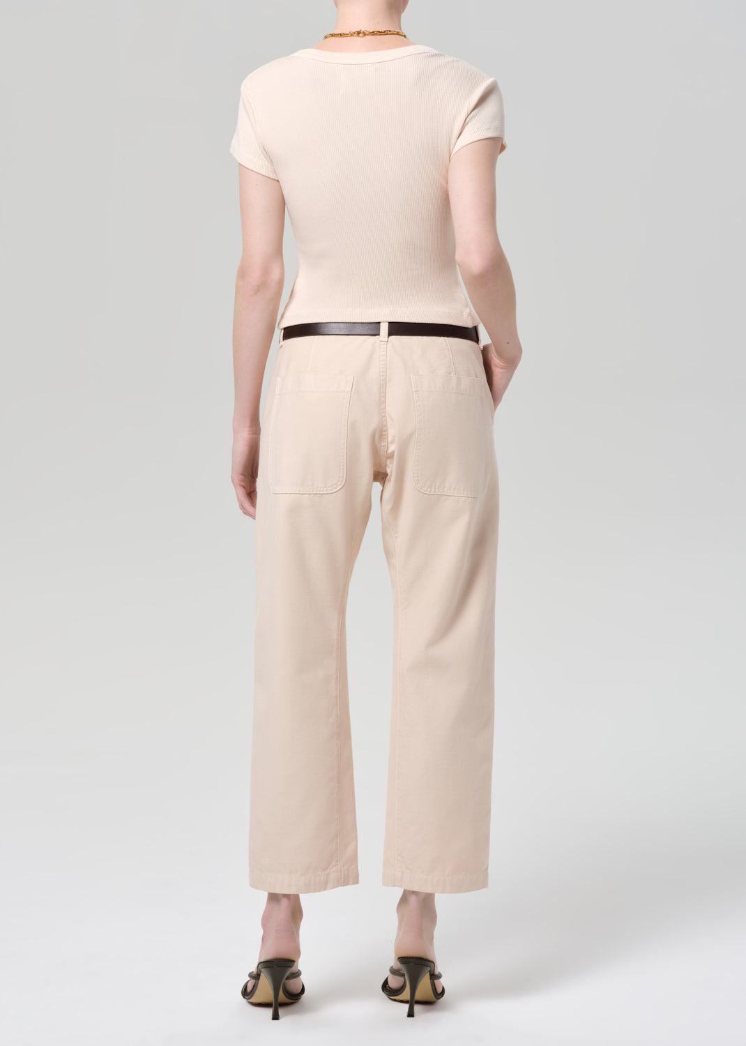 Person wearing a light peach outfit with a belt on a grey background
