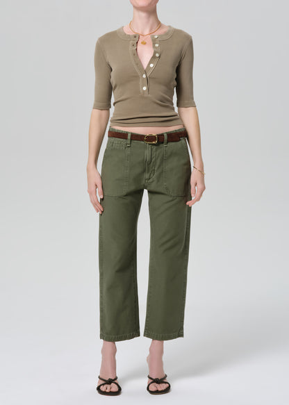 Person wearing a green top and olive green pants on a grey background