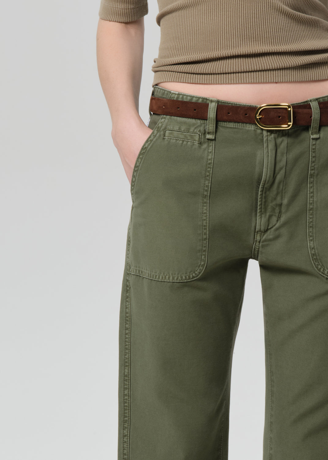 Person wearing a green top and olive green pants on a grey background
