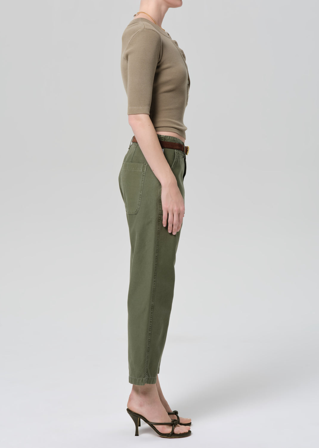 Person wearing a green top and olive green pants on a grey background