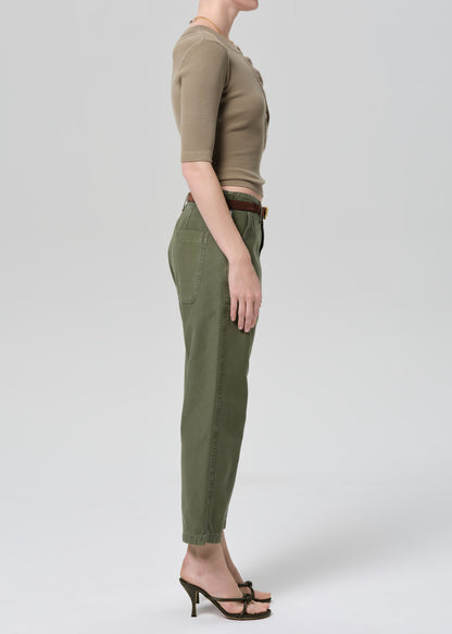 Person wearing a green top and olive green pants on a grey background