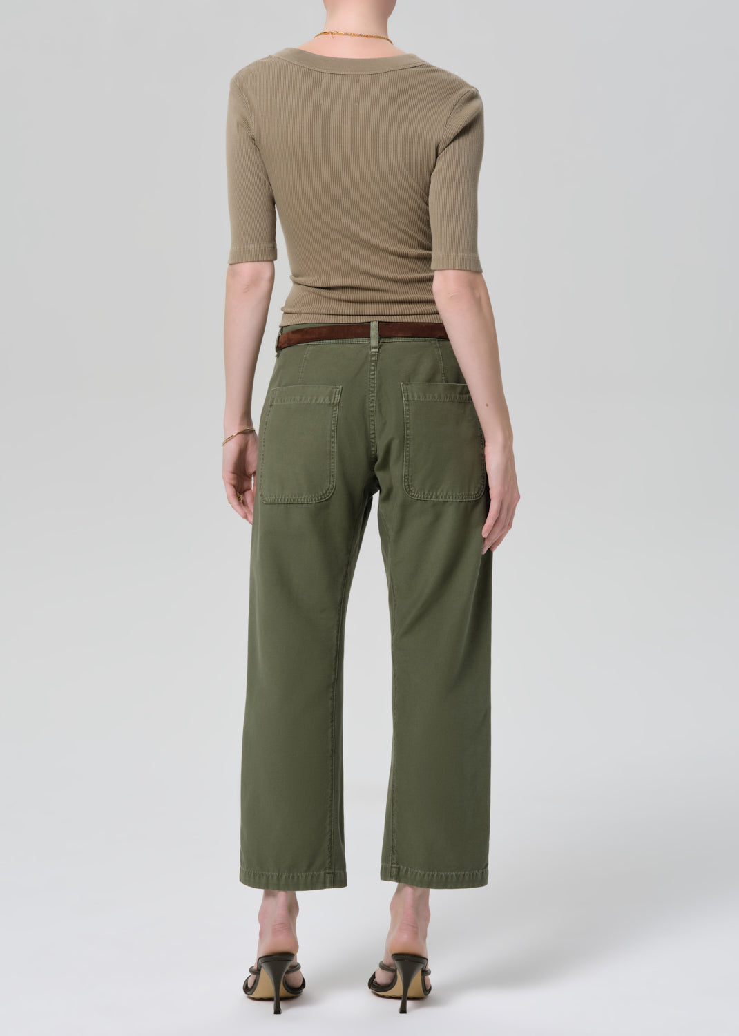 Person wearing a green top and olive green pants on a grey background