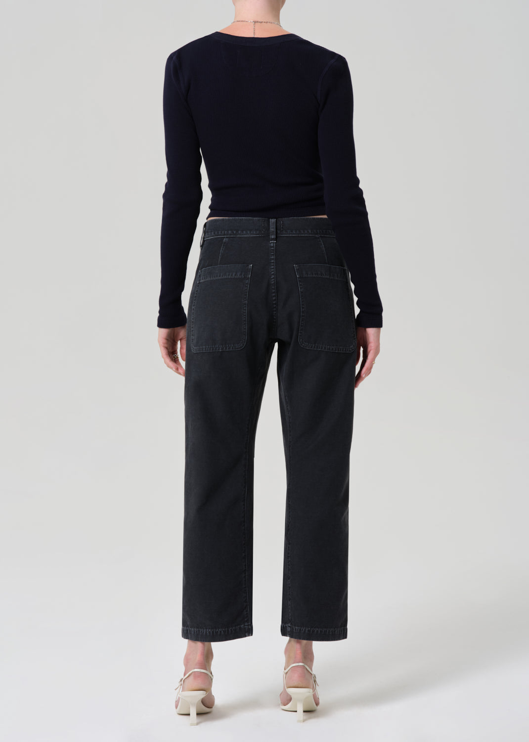 Person wearing a black long-sleeve top and black jeans on a grey background