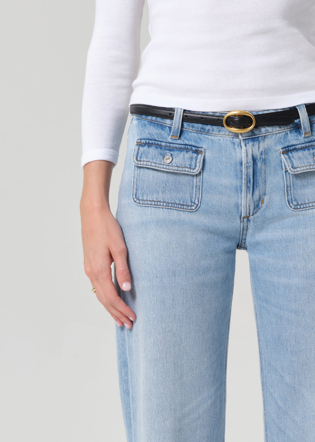 Light blue jeans with a black belt and gold buckle on a plain background
