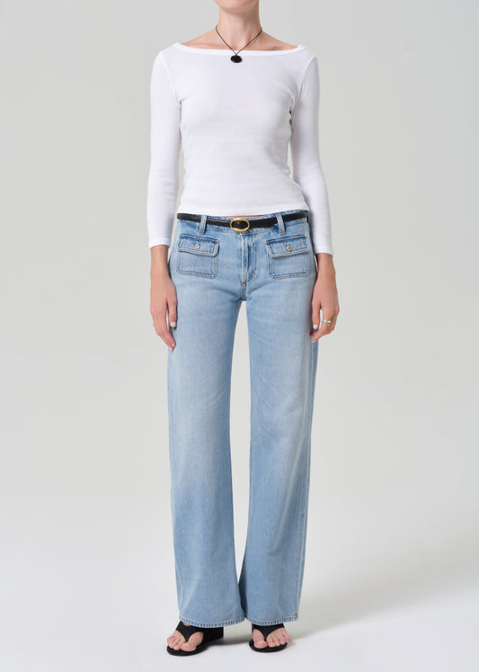 Person wearing a white long-sleeve top and light blue jeans on a plain background