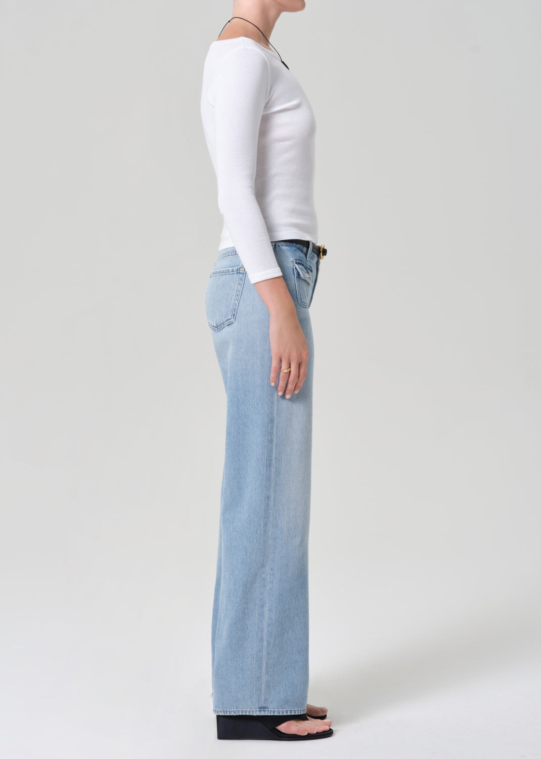 Person wearing light blue jeans and a white long-sleeve shirt on a plain background