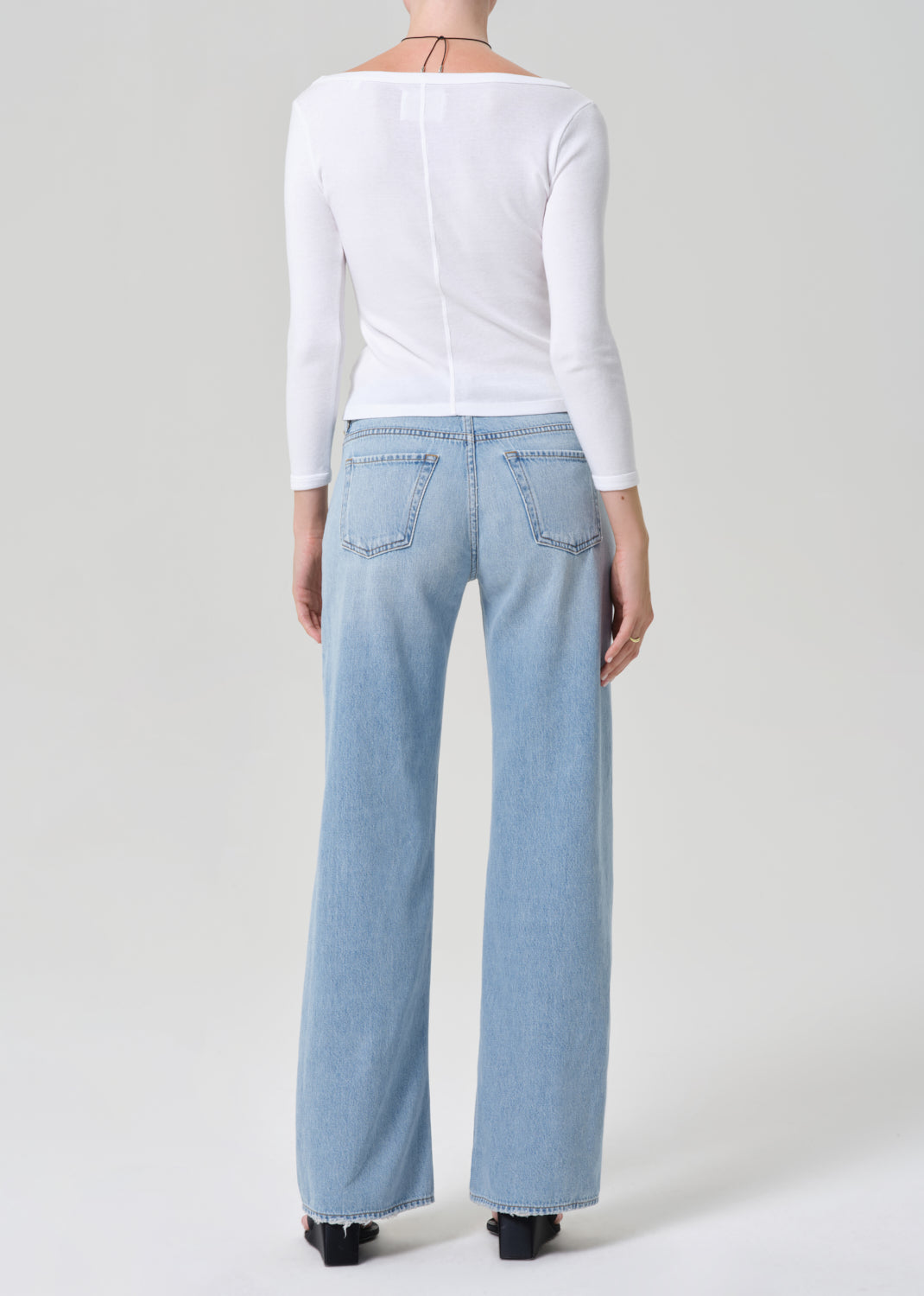 Person wearing light blue jeans and a white top on a plain background