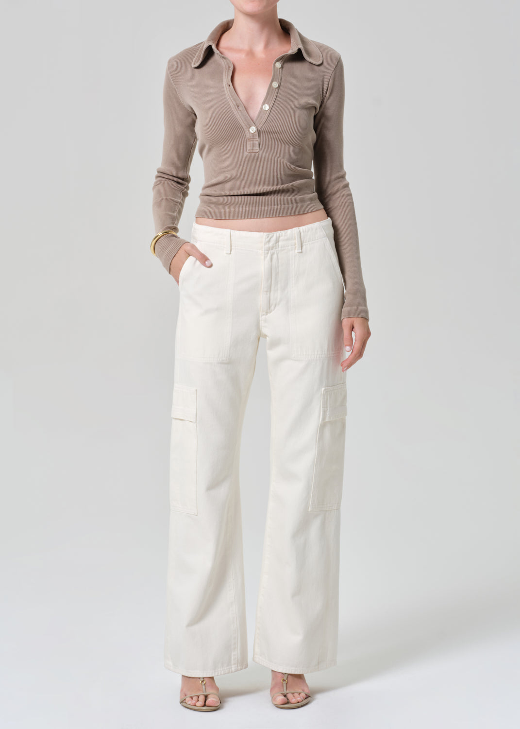 Person wearing a brown long-sleeve shirt and white pants on a light gray background