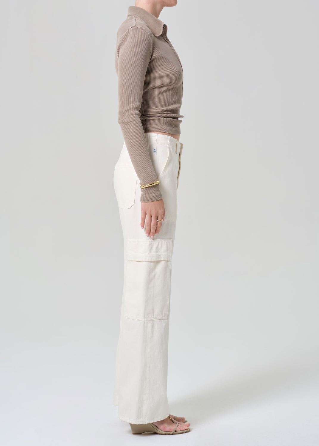 Person wearing a brown long-sleeve shirt and white pants on a light gray background