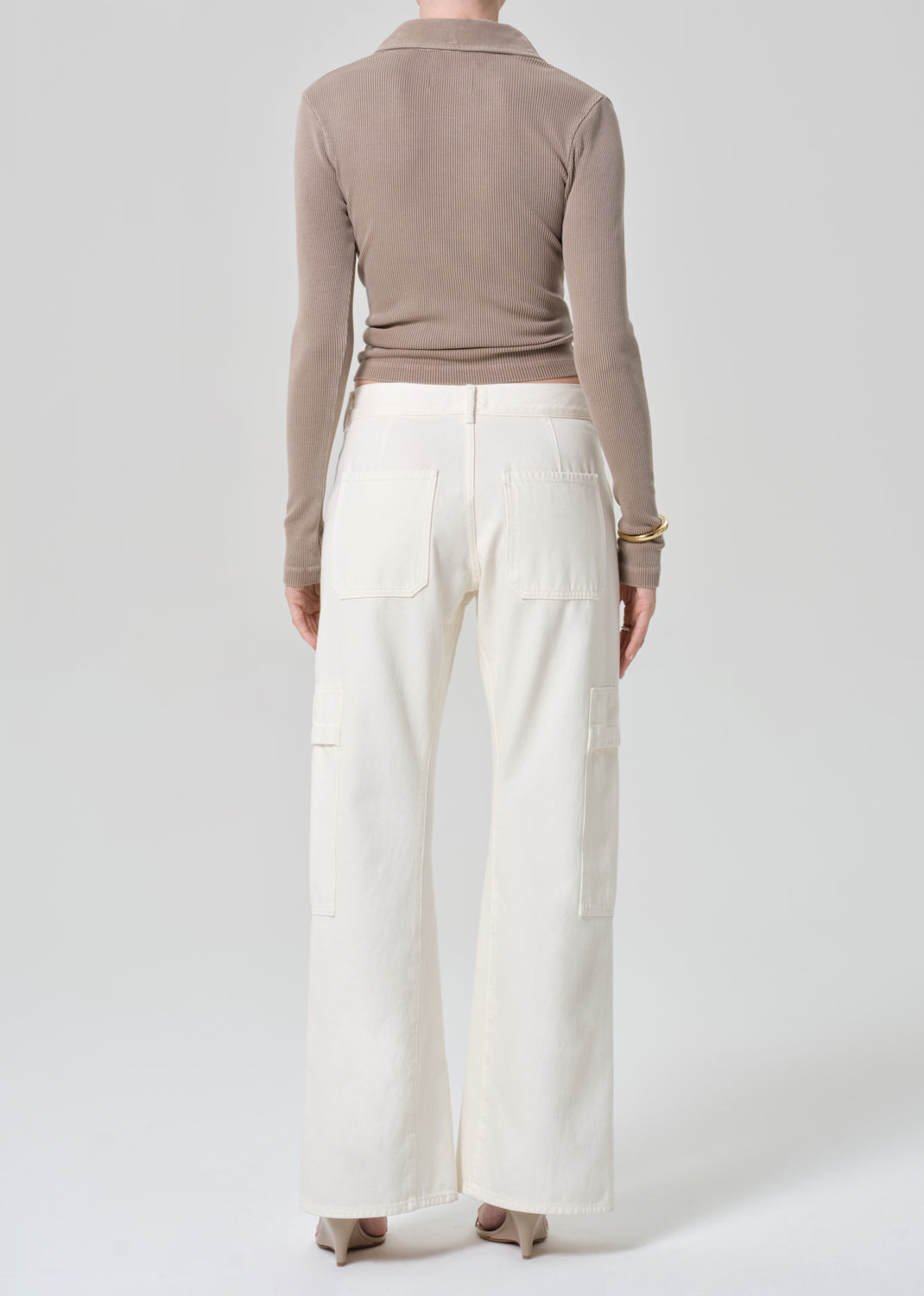 Person wearing a brown long-sleeve shirt and white pants on a light gray background