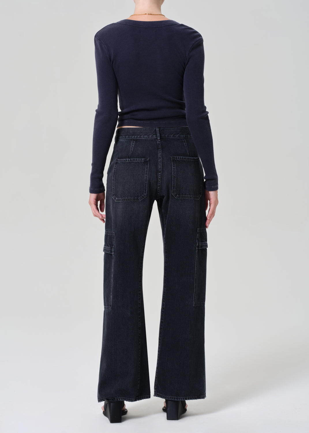 Person wearing a navy long-sleeve top and dark wash wide-leg jeans on a grey background