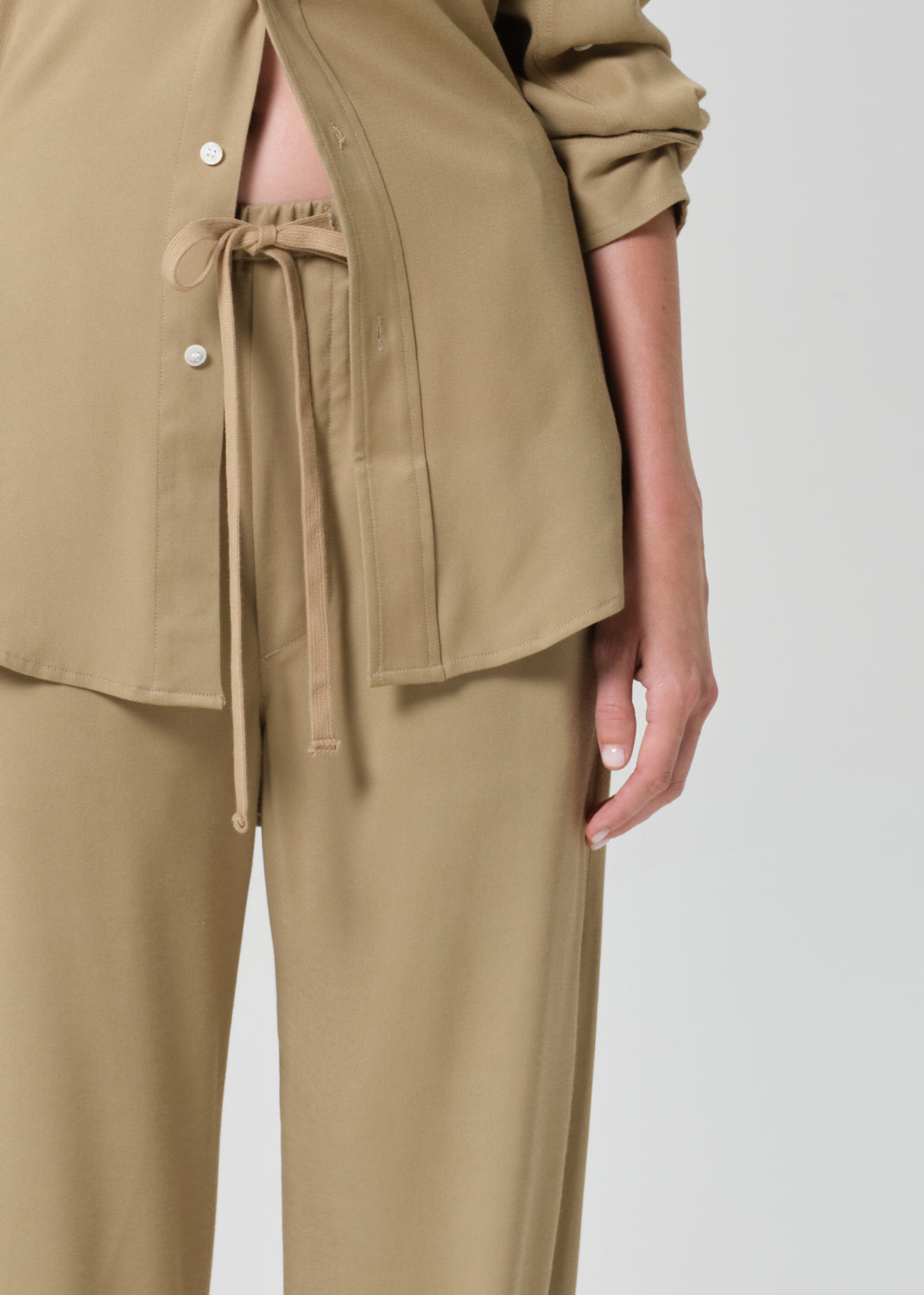 Person wearing a beige shirt and pants set on a grey background