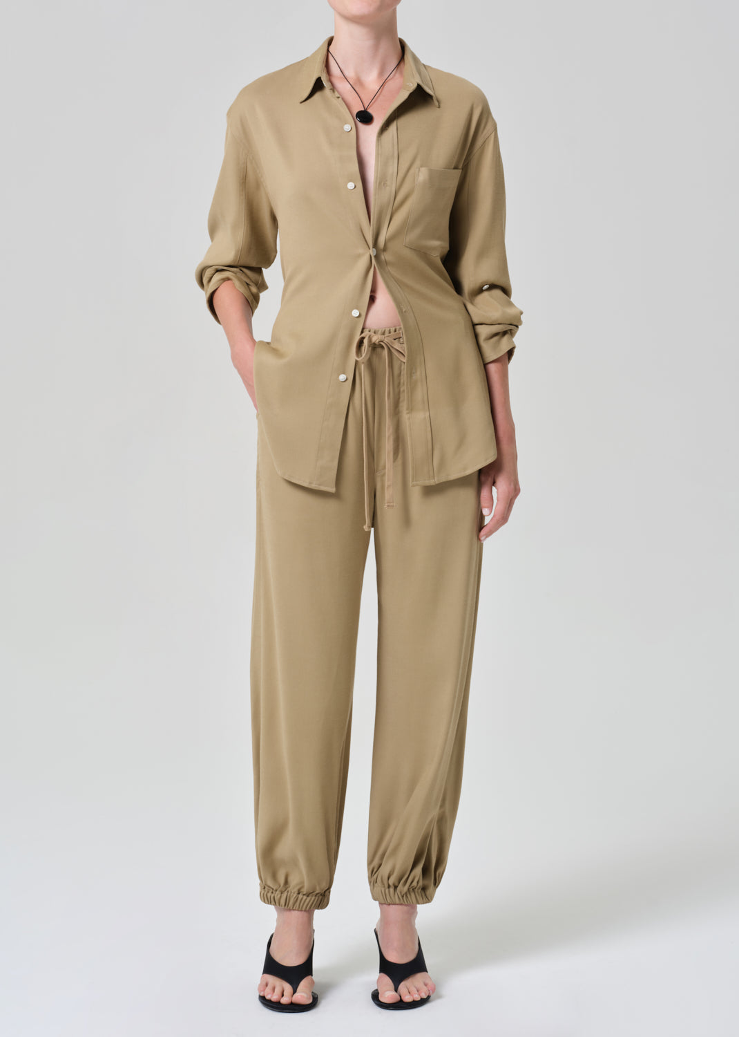 Person wearing a beige shirt and pants set on a grey background