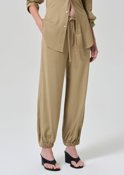 Person wearing a beige shirt and pants set on a grey background