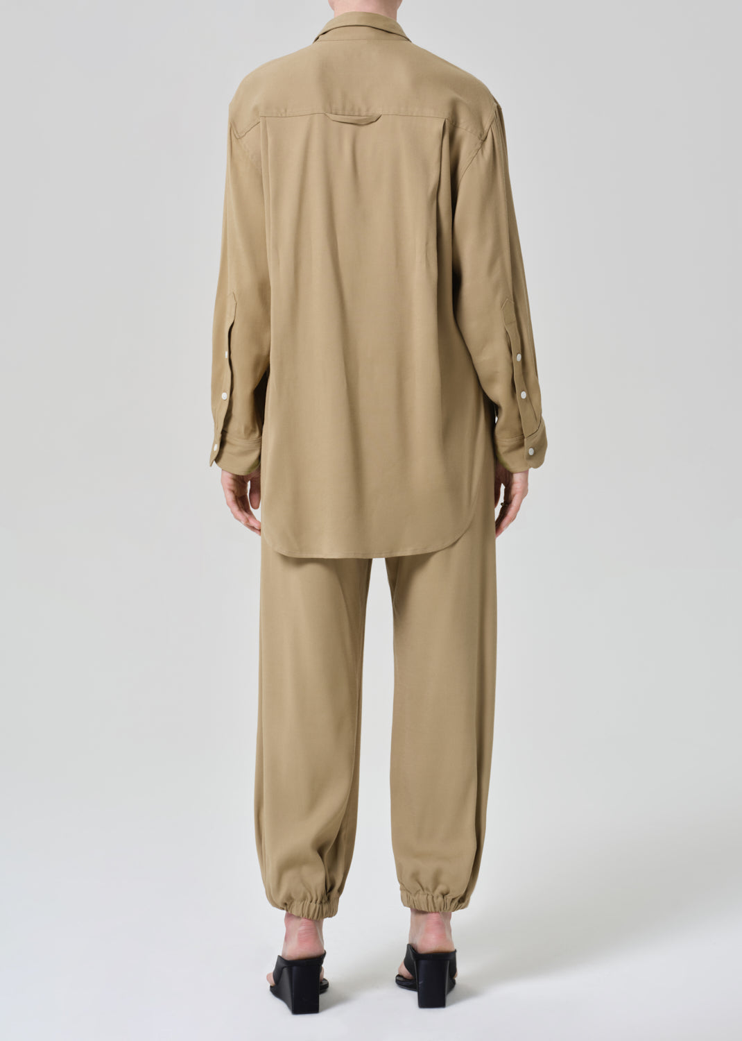 Person wearing a beige shirt and pants set on a grey background