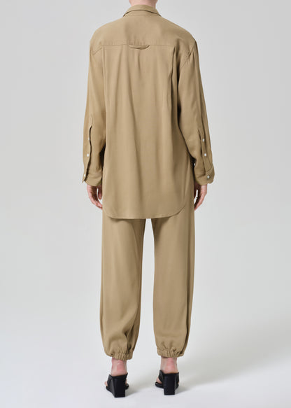 Person wearing a beige shirt and pants set on a grey background