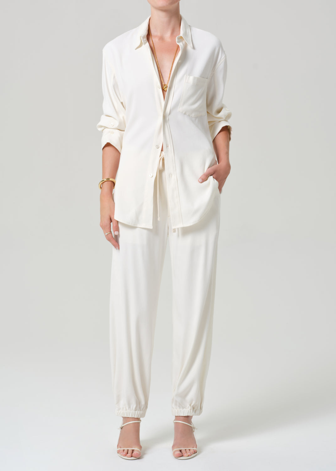 Person wearing a cream shirt and matching pants on a grey background