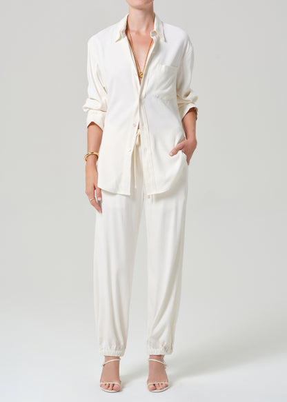 Person wearing a cream shirt and matching pants on a grey background