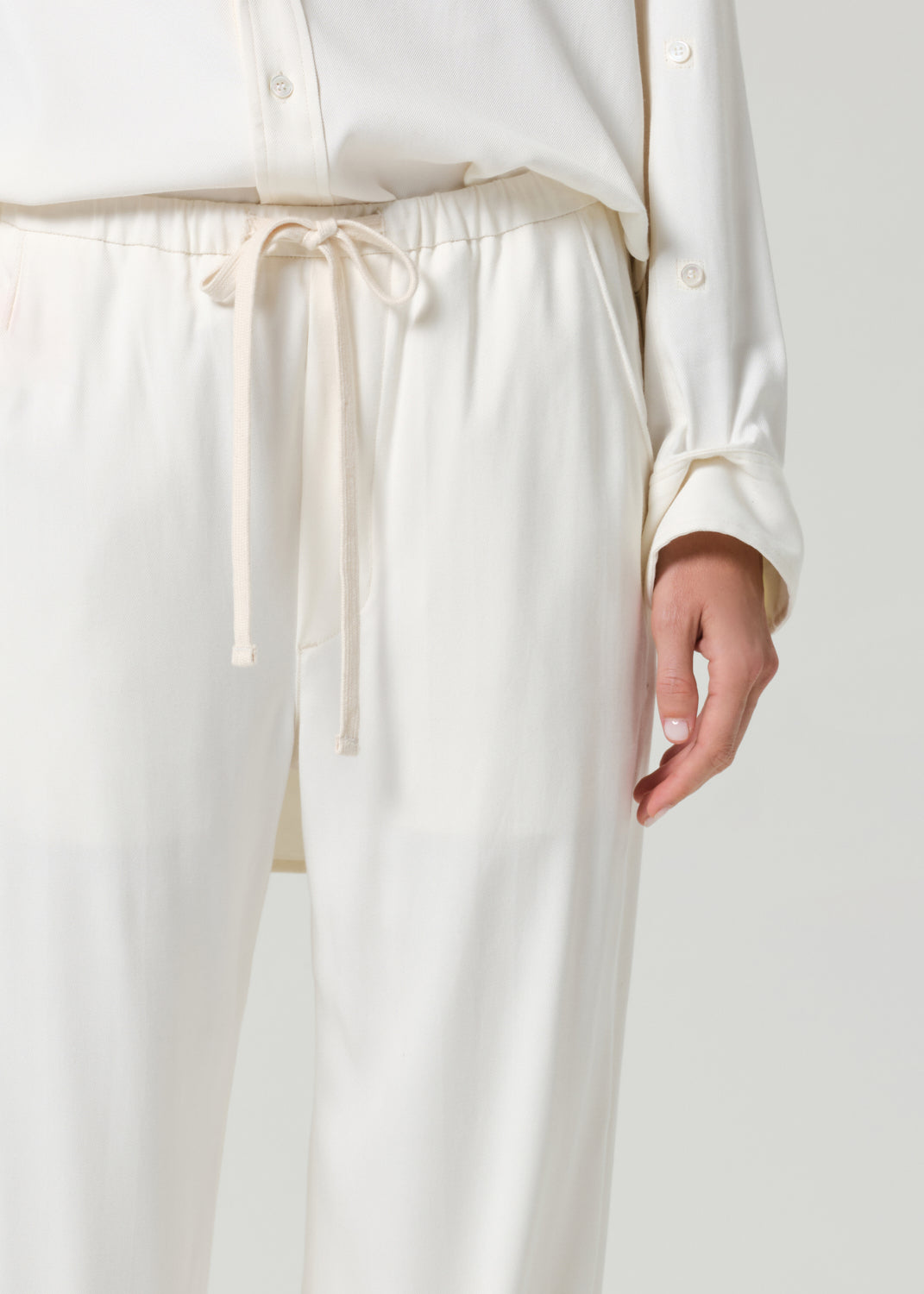 Person wearing a cream shirt and matching pants on a grey background