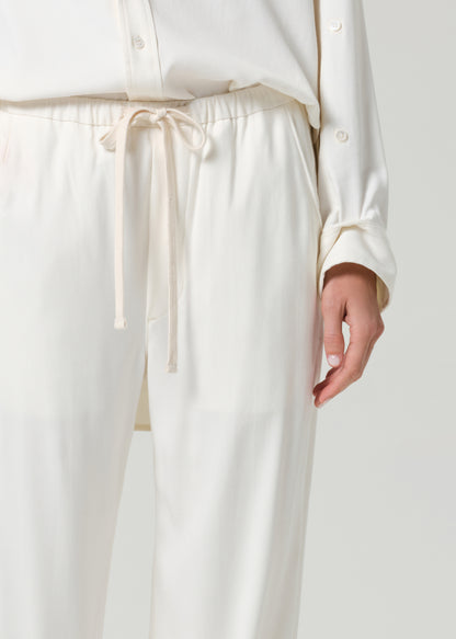 Person wearing a cream shirt and matching pants on a grey background