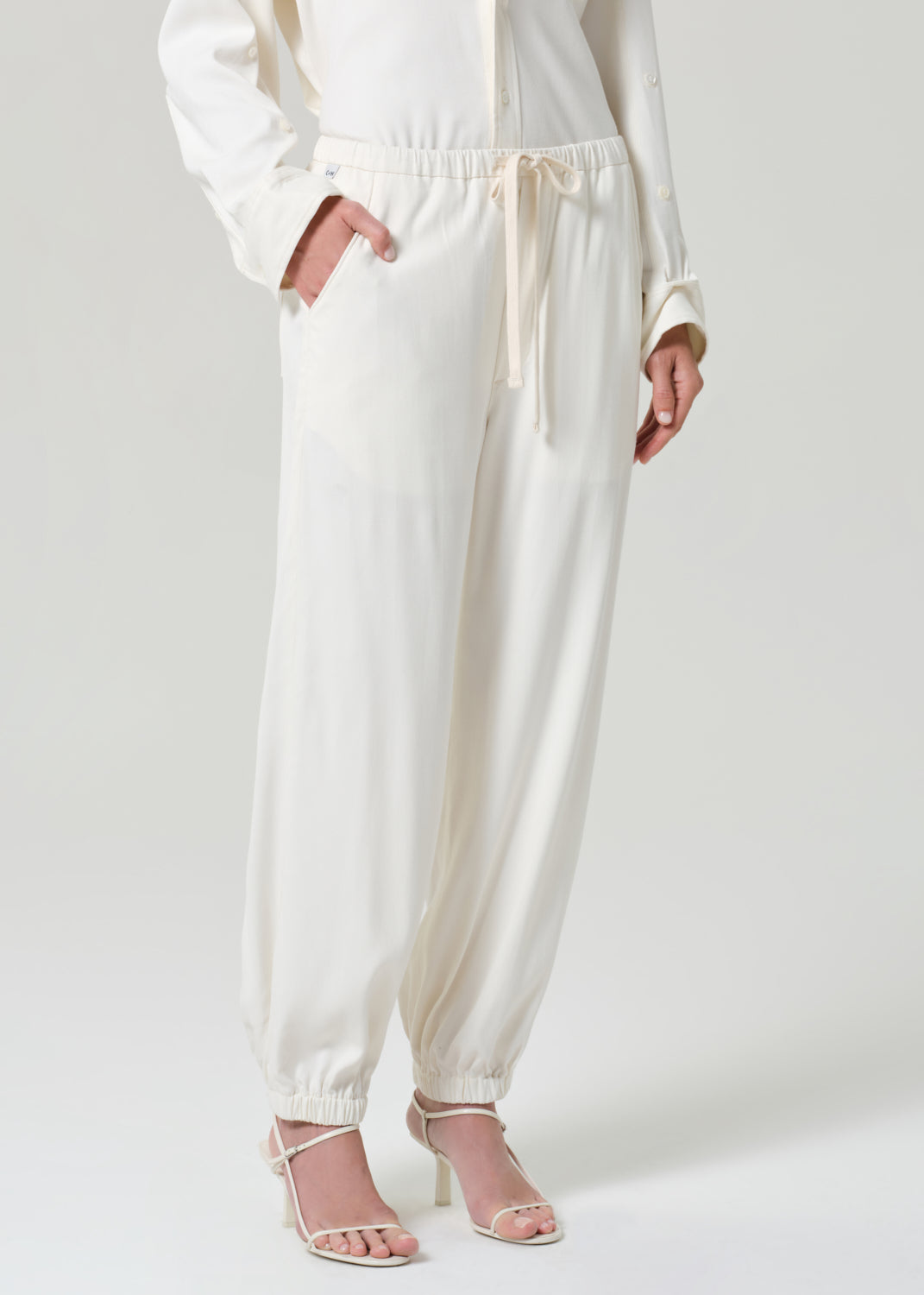 Person wearing a cream shirt and matching pants on a grey background