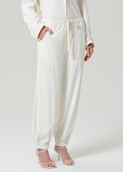 Person wearing a cream shirt and matching pants on a grey background