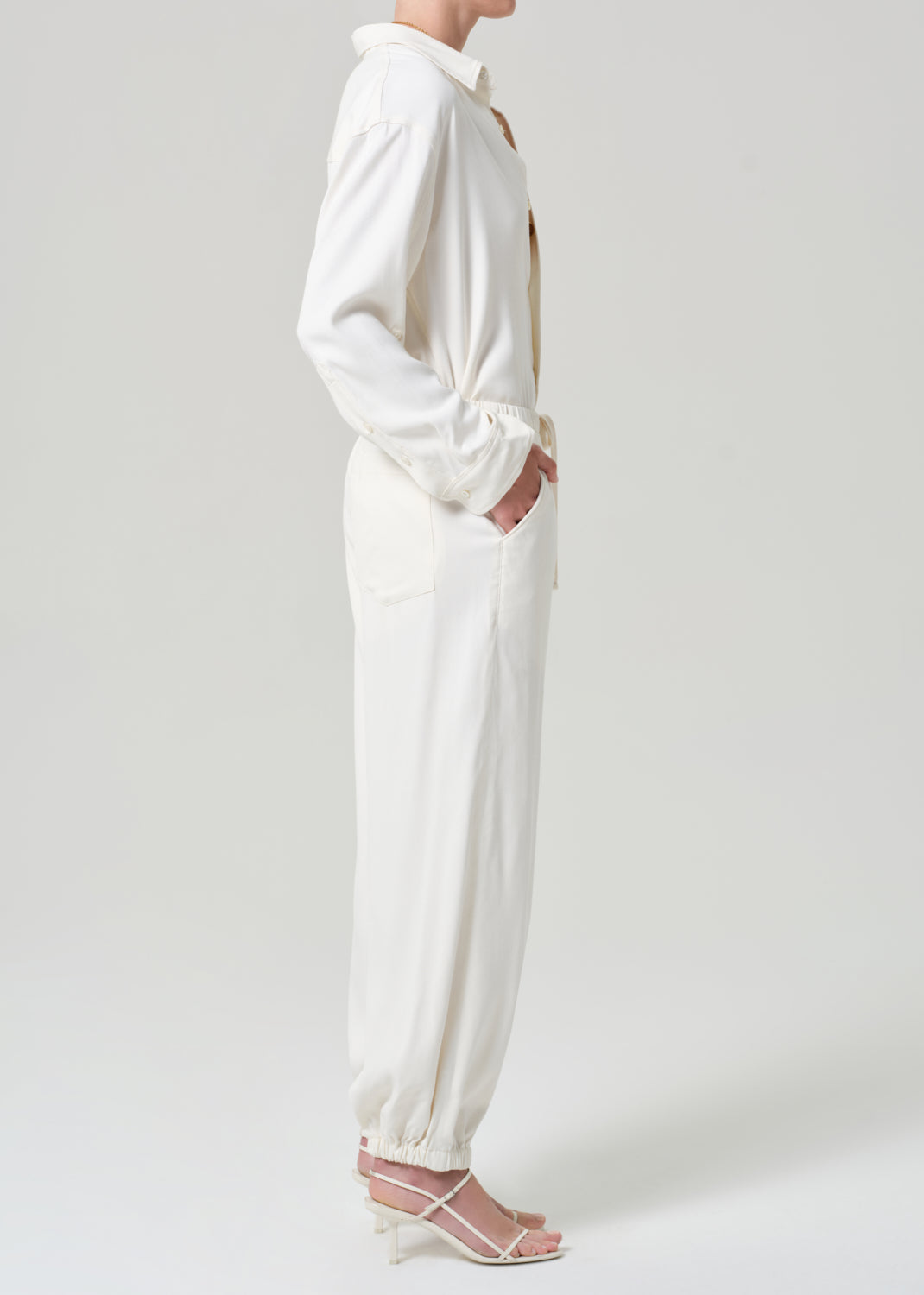 Person wearing a cream shirt and matching pants on a grey background