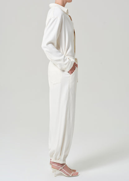 Person wearing a cream shirt and matching pants on a grey background