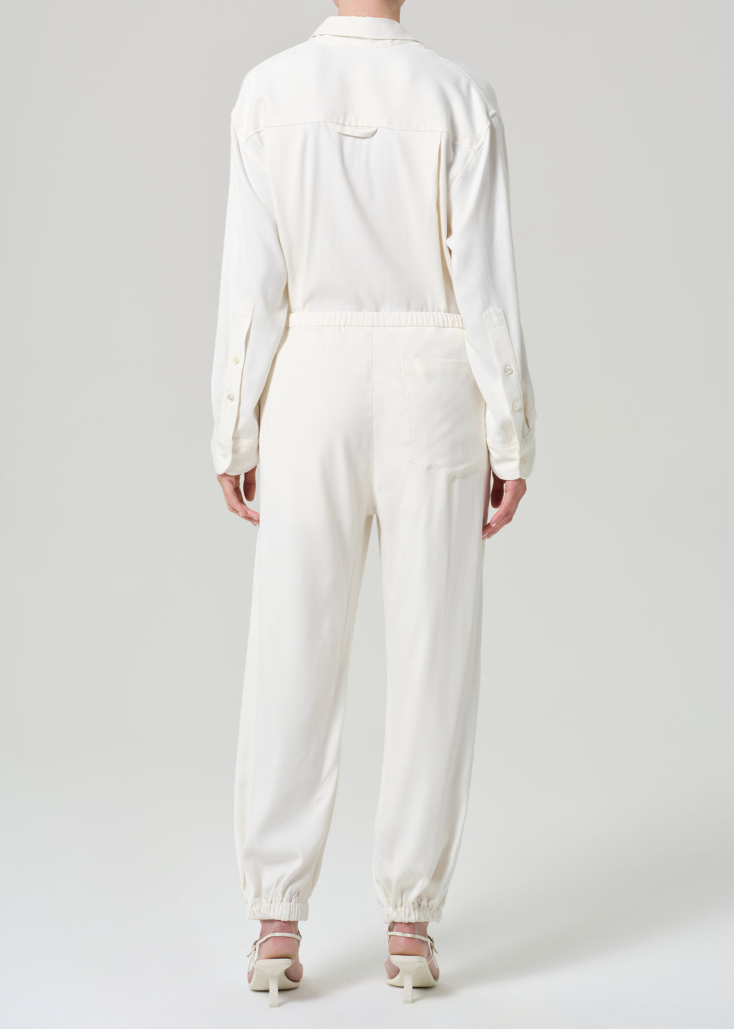 Person wearing a cream shirt and matching pants on a grey background